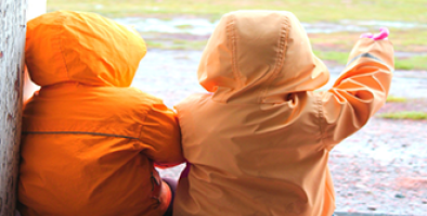 Two children in raincoats looking at a rainy field