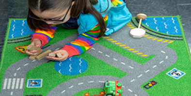 A little girl playing on a rug with roads printed on it