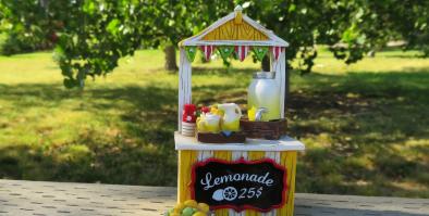 Yellow lemonade stand with trees and grass in the background.