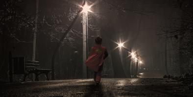 boy in superman cape walking on a dark street