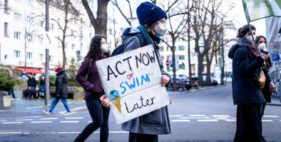 Photo of protester holding sign reading "Act Now or Swim Later"