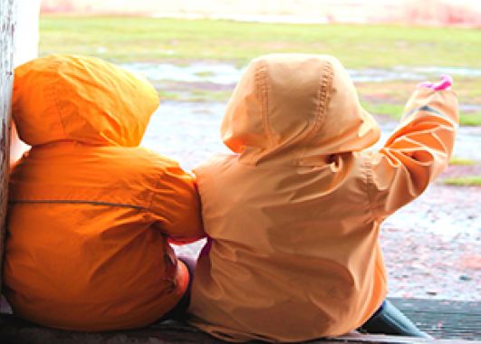 Two children in raincoats looking at a rainy field