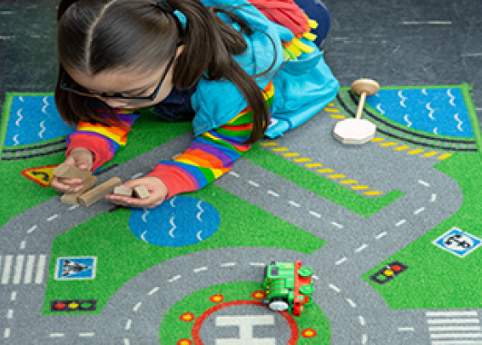 A little girl playing on a rug with roads printed on it