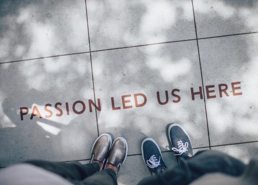 two people looking down at the sidewalk, where the words: passion led us here are placed.