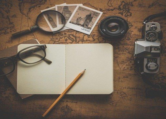 photo of notebook, camera, photos with magnifying glass and glasses scattered on top of a map.