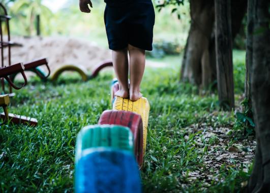 Child standing on a tire that is painted yellow. The yellow tire is 4th in line after a blue, green and red tire.