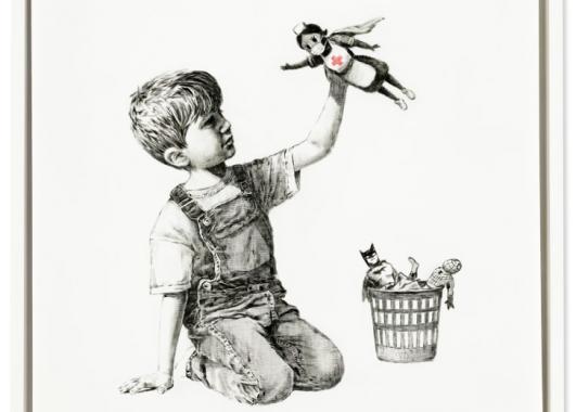 A child holding up a toy that portrays a nurse as a superhero. 
