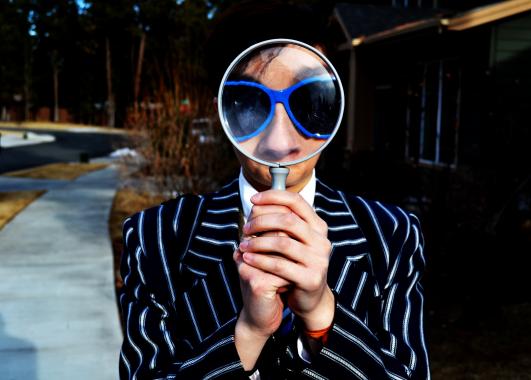 Person with magnifying glass held in front of their face.