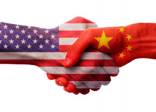 two hands, each painted like the flag of the USA and China, shaking in greeting.