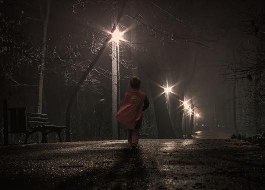 boy in superman cape walking on a dark street