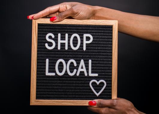 hands holding a square sign with a black background white text shop local with a heart